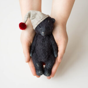 Filz-Elfenpuppe mit Hut auf schwarzem Teddybär in den Händen