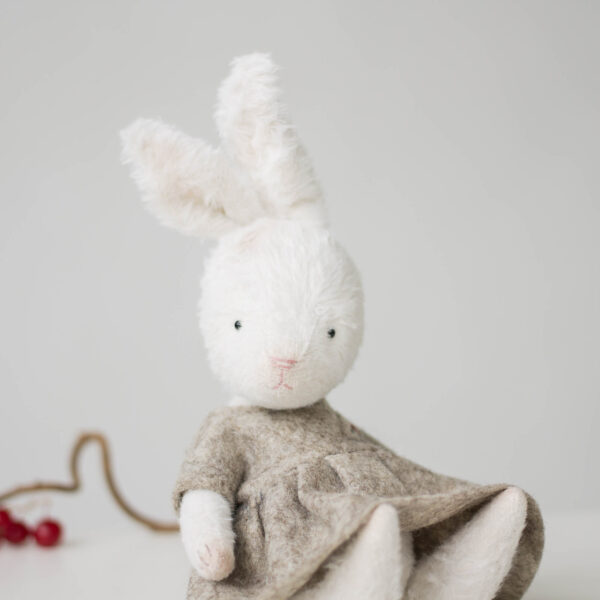 white plush bunny rabbit in felt doll dress sitting on shelf