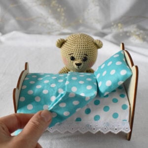 Soft toy bear beige color. Next to a wooden bed with a set of bed linen. On the bed there is a mattress, a sheet, a pillow, a blanket.