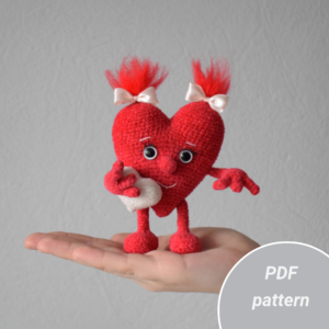 Soft sculpture of the heart. It stands on the palm of your hand. The figure holds a small heart in its hands. On the head hairstyle two tails with bows.