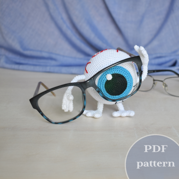 Crocheted eye. Standing on his feet. He holds large glasses with one hand