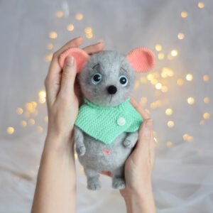 Une souris grise en peluche. Un jouet sur un cadre. Un foulard turquoise avec un bouton sur le cou.