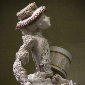 An artistic doll of a girl from the 19th century in a beautiful dress and hat with shopping and an umbrella.