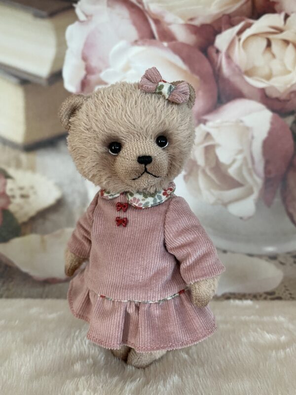 Miniature beige teddy bear in pink dress