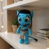 A handmade crochet doll inspired by the Na’vi from the movie Avatar. The blue-skinned character features long black braids, pointed ears, glowing yellow eyes, and tribal clothing with detailed accessories. This amigurumi doll captures the essence of Pandora’s native species in a soft, artistic style.