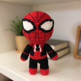 A handmade crochet doll of Spider-Man from Marvel, featuring his classic red and blue suit with black web detailing and large white eyes. This soft amigurumi superhero is designed as a plush toy and stands upright on a neutral surface.