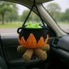 Crocheted witch cauldron amigurumi with green potion and flames, hanging in a car as Halloween decoration.