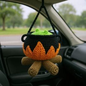 Crocheted witch cauldron amigurumi with green potion and flames, hanging in a car as Halloween decoration.