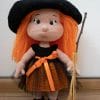 Crochet cute witch doll with very detailed body. She has 5 fingers on each of her hands, belly button and nicely shaped back bottom. Her face is also very well shaped with green safety eyes. This Halloween decoration doll is a dress up doll. She wears a black and orange dress. The bottom part is orange color and on top of it, the dress is finished with a black tule fabric. The dress has an orange ribbon tied on under the bust. This amigurumi witch doll wears black shoes closed with stripes and black buttons. The witch's long hair is made of orange yarn. On top of the head she wear a black witch hat with an orange ribbon. This Halloween witch has a broom made of natural materials and there is a loop on one of the hands where the broom can be placed to create the illusion of holding.